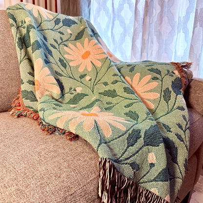Floral patterned throw blanket draped over a couch with a window in the background.