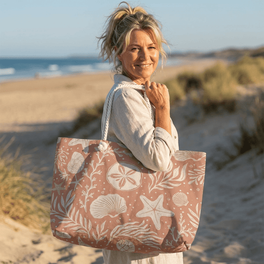 Woman holding a beach bag with a shell pattern on a sandy beach.